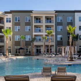 Resort-Style, Saltwater Pool with Sun Shelf and Underwater Benches Dog-Friendly Luxury Apartments in Savannah, GA - Aventon Victory - Resort-Style Pool with Saltwater, with Sun Shelf, Umbrellas with Table and Chairs Surrounded by Tanning Lounge Chairs with Palm Trees