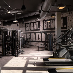 State-of-the-Art Fitness Center with Cardio and Strength Training 1-Bedroom Luxury Apartments in Savannah, GA - Aventon Victory - Fitness Center with Cardio Machines, Strength Training Machines, a Tall Ceiling with Ceiling Fans, and Large Windows